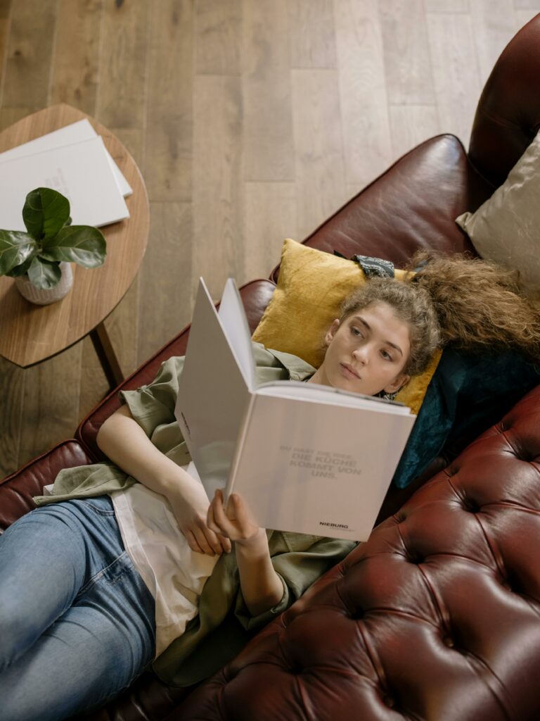 Young woman relaxing and reading a book on a leather sofa indoors.
