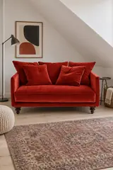 Vue d'ensemble du canapé Lazare La Redoute 2 places en velours, coloris rouge cinabre, style classique, dans un petit séjour sous les toits (mise en situation illustrée par IA)