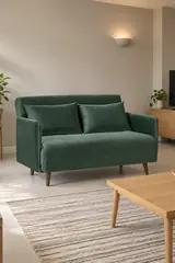 Vue d'ensemble du canapé Belushi Maisons du Monde 2 places convertible en velours, coloris vert forêt, style contemporain, dans un séjour familial aux murs greige (mise en situation illustrée par IA)